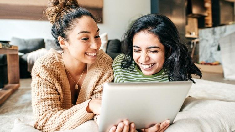 zwei junge frauen schauen gluecklich auf ein tablet